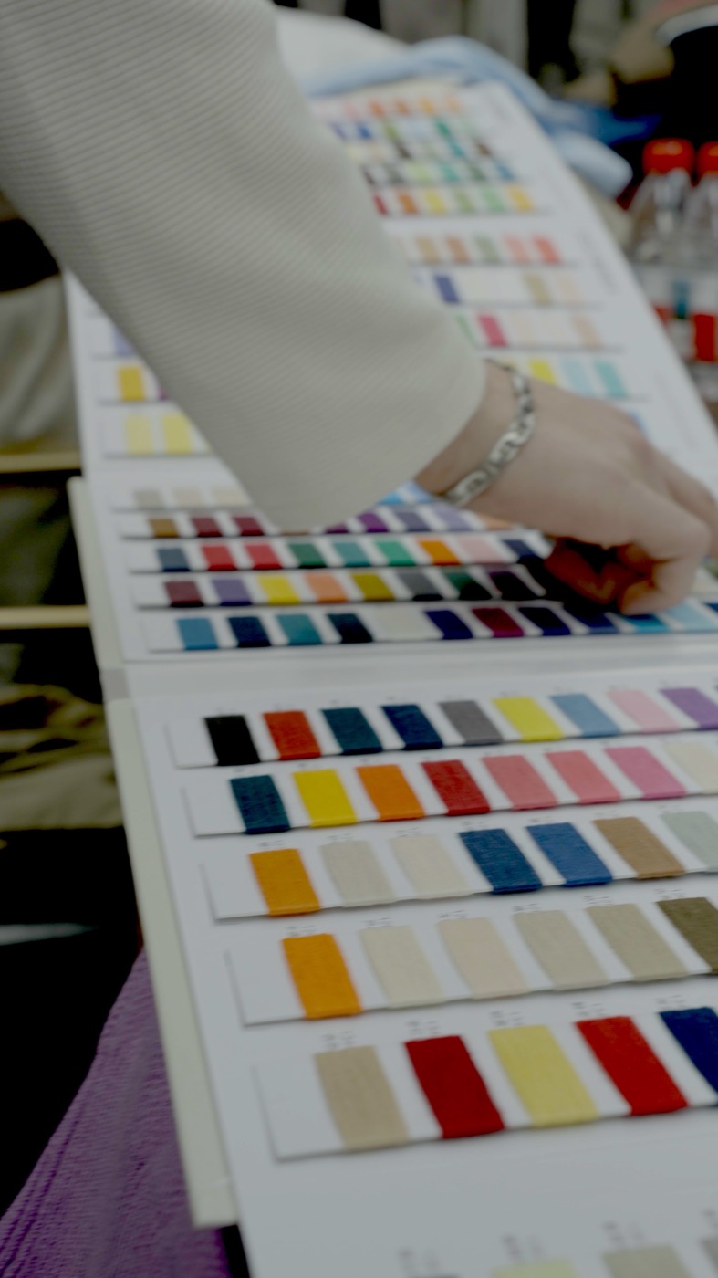 A hand rests on an open yarn colour card covered in rows of woven swatches