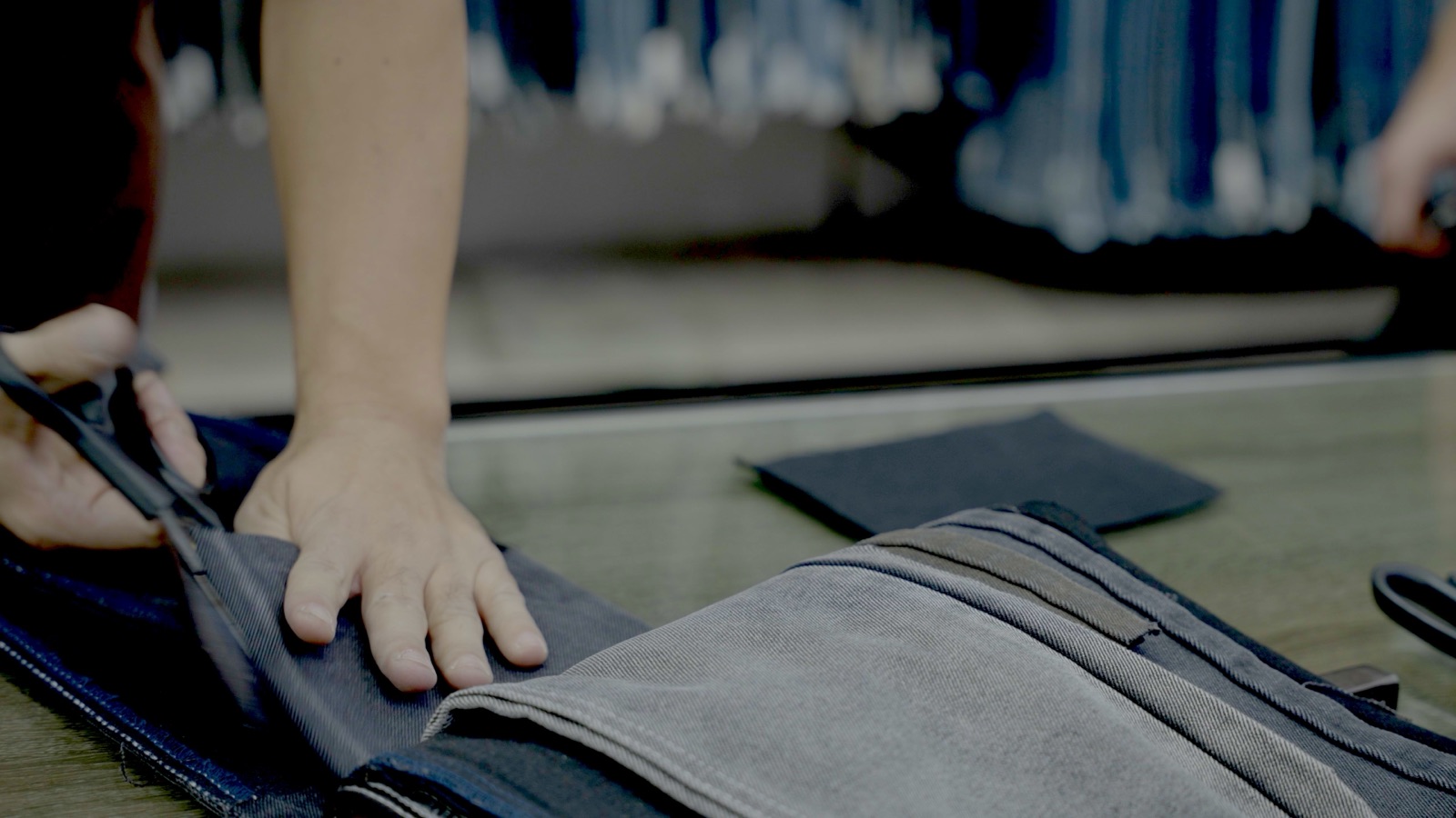 A hand presses denim swatches flat on a supplier counter at the fabric market